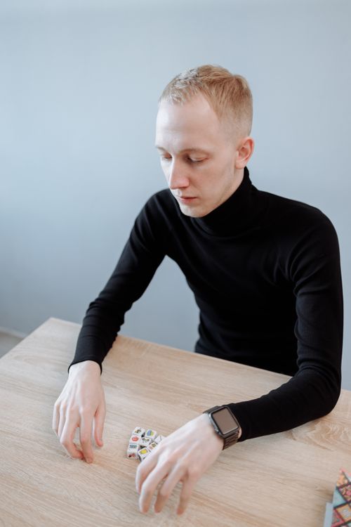 Free Young caucasian man in black sweater rolling dice on a wooden table indoors. Stock Photo