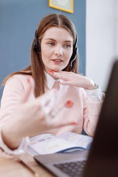 Woman wearing headset teaches online using a laptop from home, engaging in a virtual lesson.