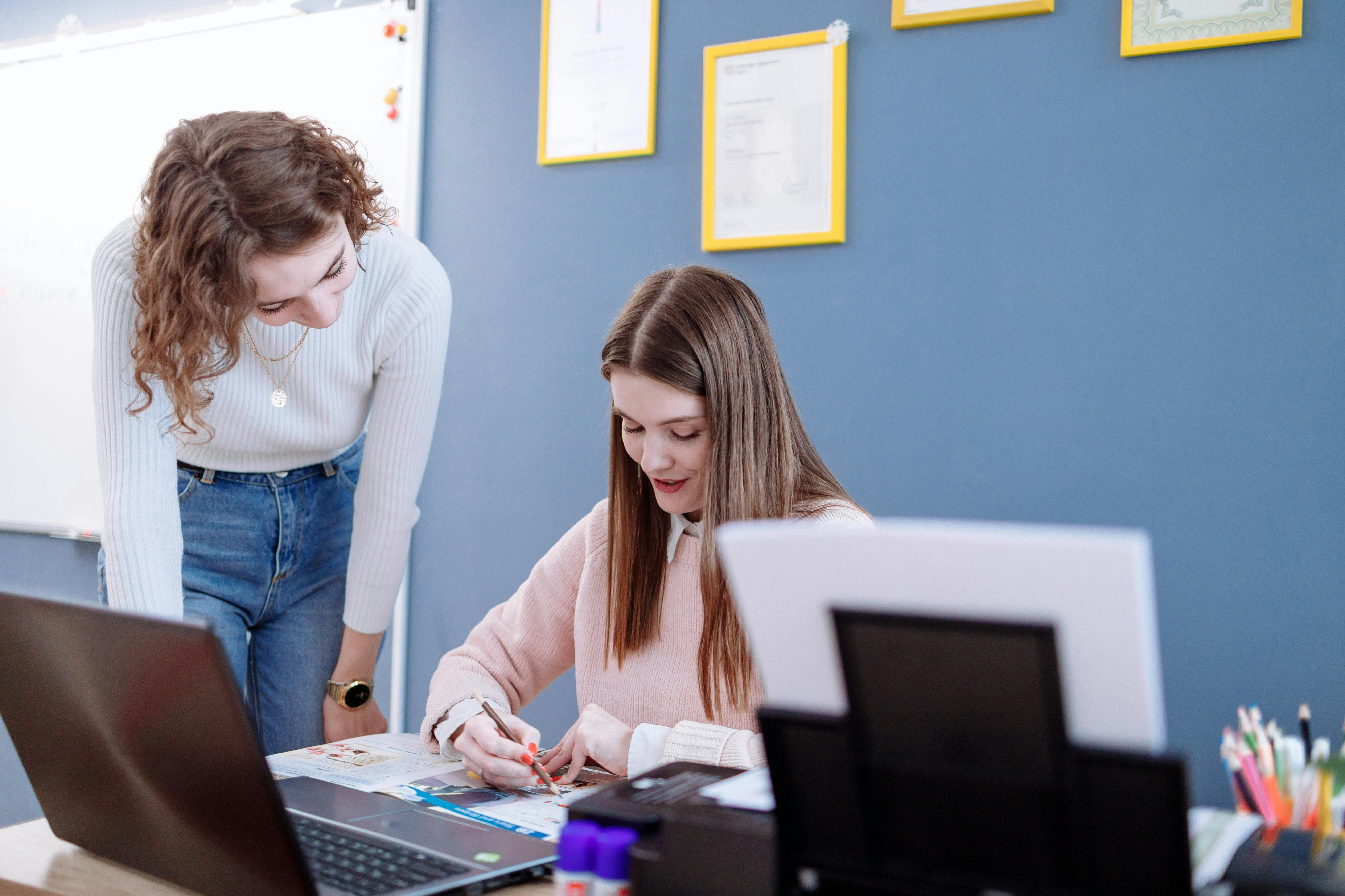 Two women working together on educational materials in a classroom setting.