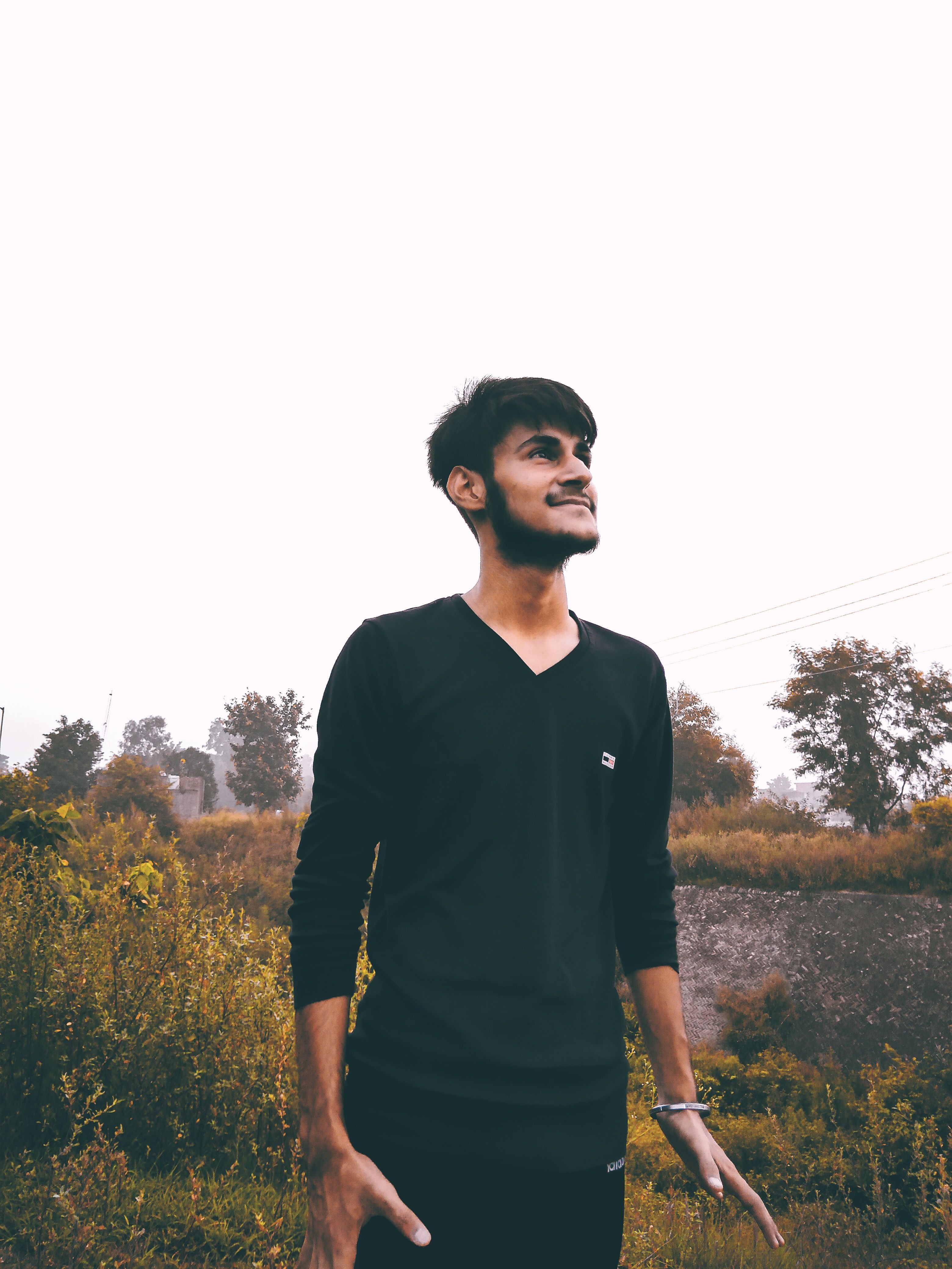 A cheerful man smiling outdoors in a natural setting wearing black long sleeves.
