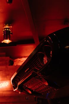 Close-up of a classic car bumper under red neon light in a retro setting.