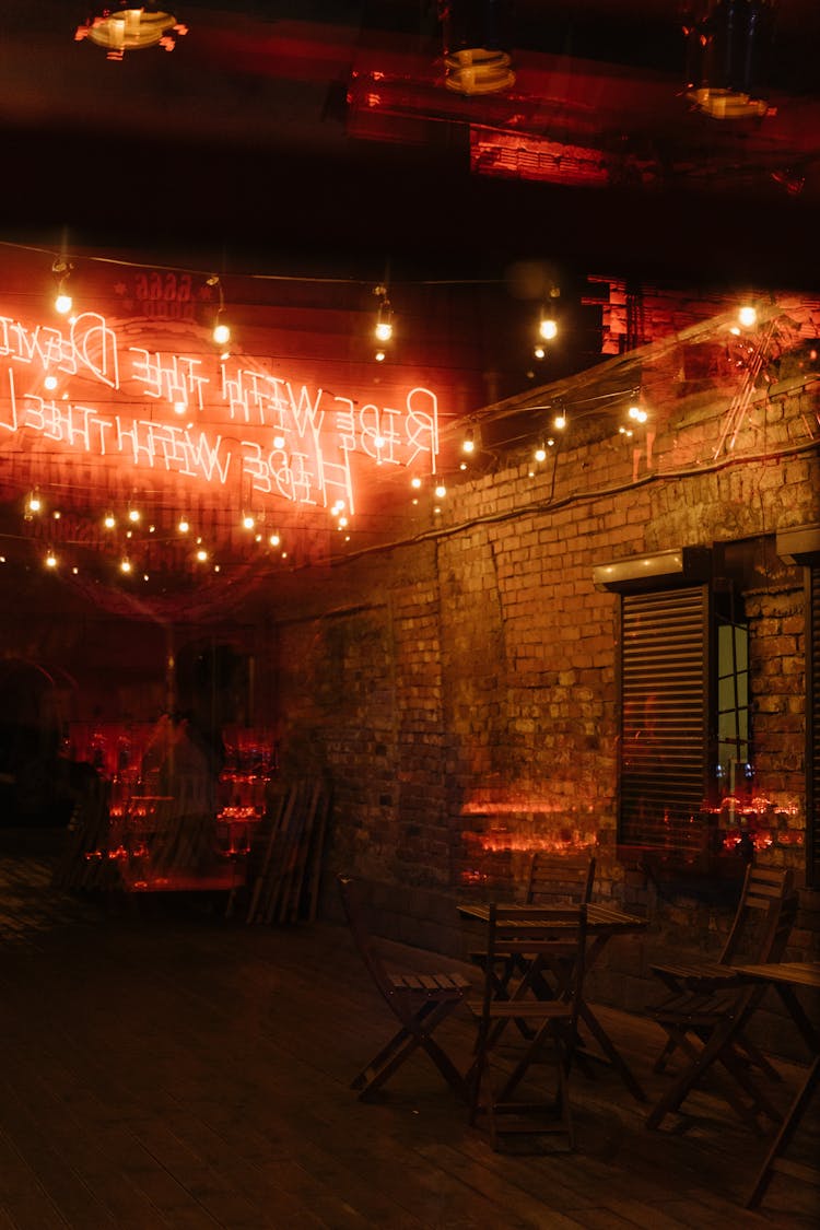 Bar With Wooden Chairs And Tables And Illuminated Neon Sign