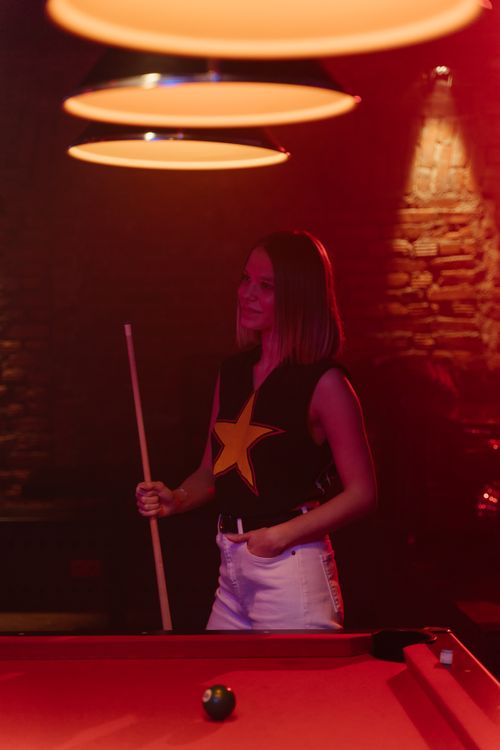 Free Young woman enjoying a game of billiards in a stylish bar with moody lighting. Stock Photo