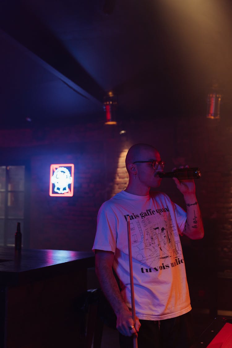 A Man Holding A Cue Stick While Drinking Bottled Beverage