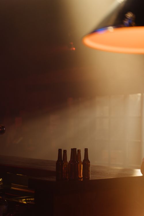 Free Cozy bar interior with beer bottles on counter and soft, moody lighting. Stock Photo
