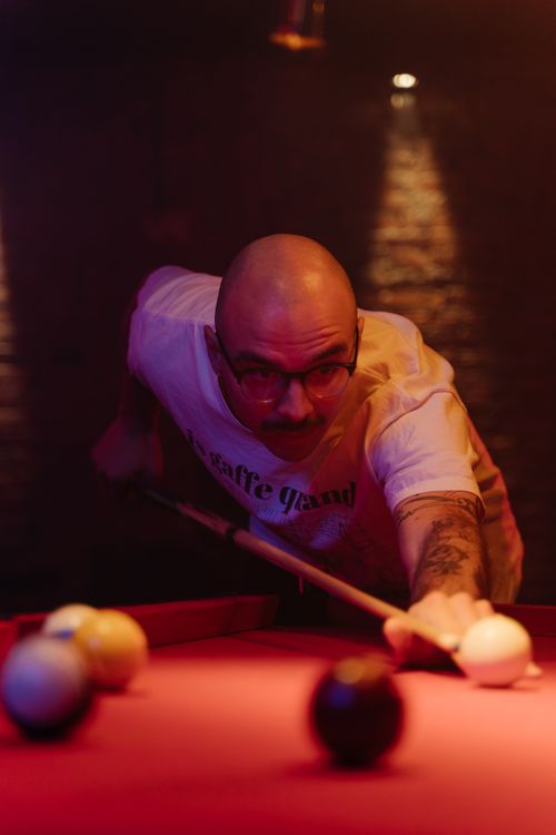 Free Bald man aiming at cue ball in a dimly lit bar setting, evoking concentration and skill. Stock Photo