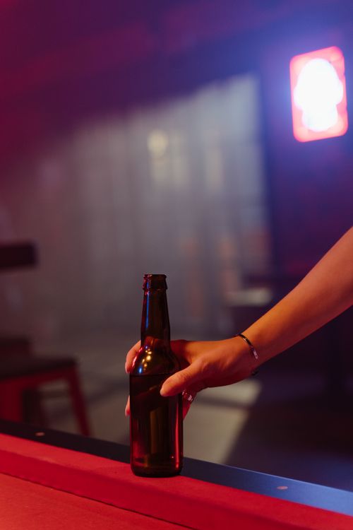 Free Hand holding a beer bottle on a billiard table in a dimly lit bar setting. Stock Photo