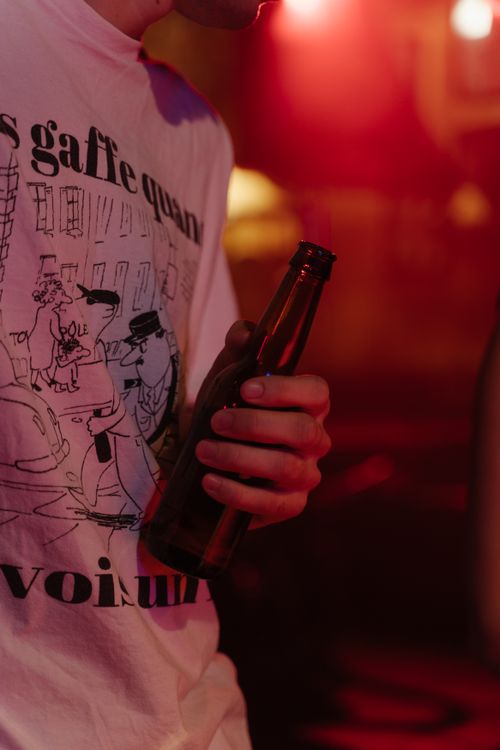 Free Close-up of a young adult holding a beer bottle in a dimly lit nightclub setting. Stock Photo