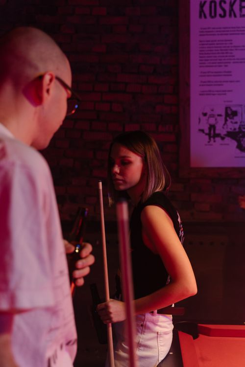 Free Charming night scene of a young couple playing billiards in a lively bar setting. Stock Photo
