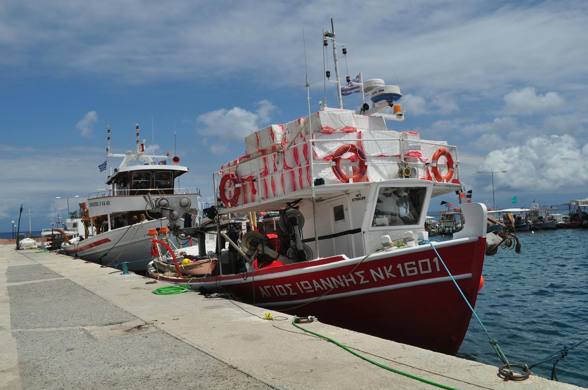 Fishing boats docked at a marina with lifebuoys and ropes against a cloudy sky.