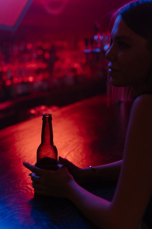 Free Silhouette of a woman holding a drink at a bar with red ambient lighting. Stock Photo