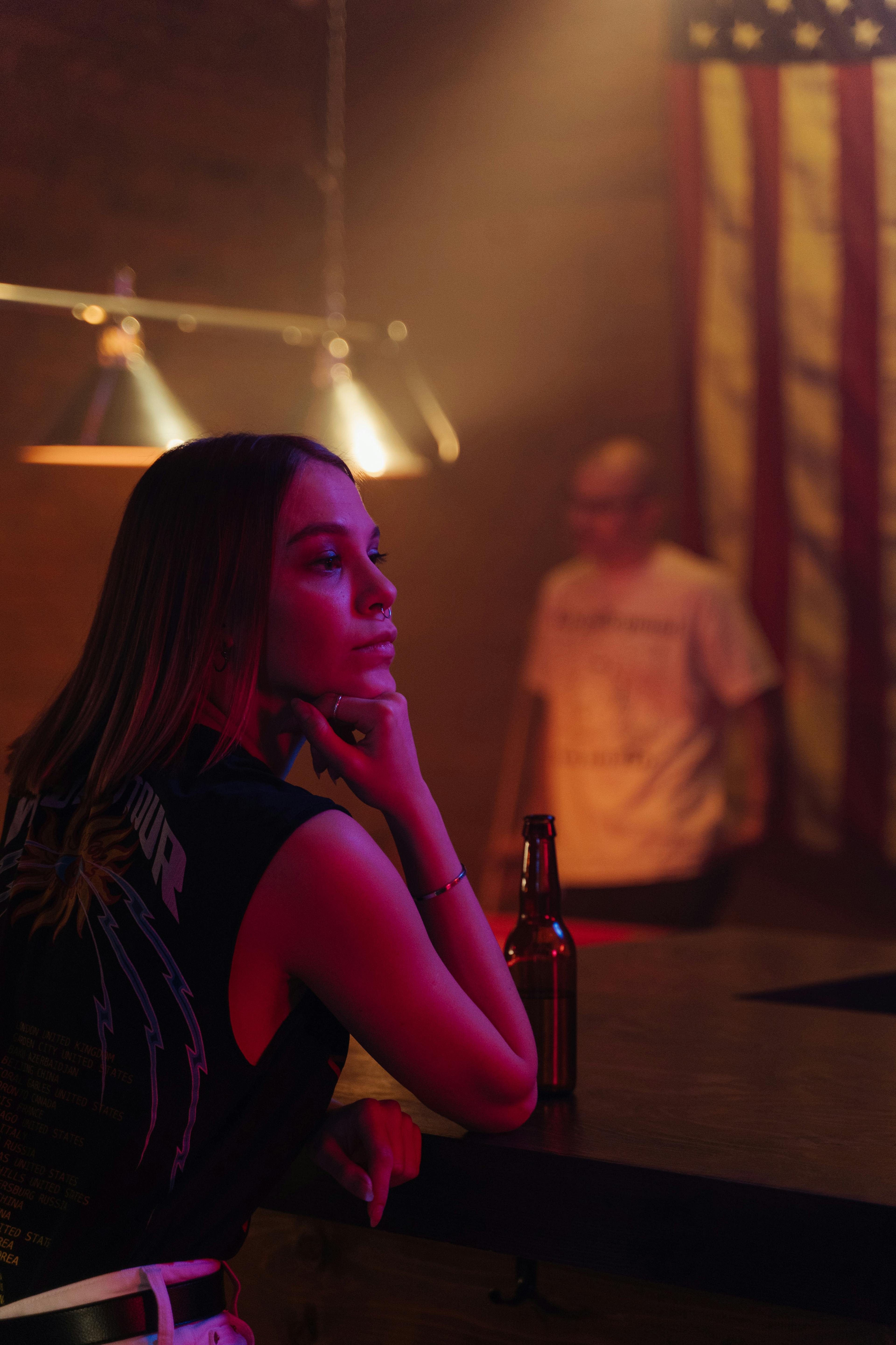 A Woman Holding a Beer Bottle by the Bar Counter