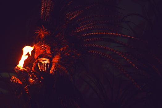 A person in a feathered headdress holding fire in the dark, evoking mystery and intrigue.