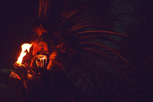 Free A person in a feathered headdress holding fire in the dark, evoking mystery and intrigue. Stock Photo