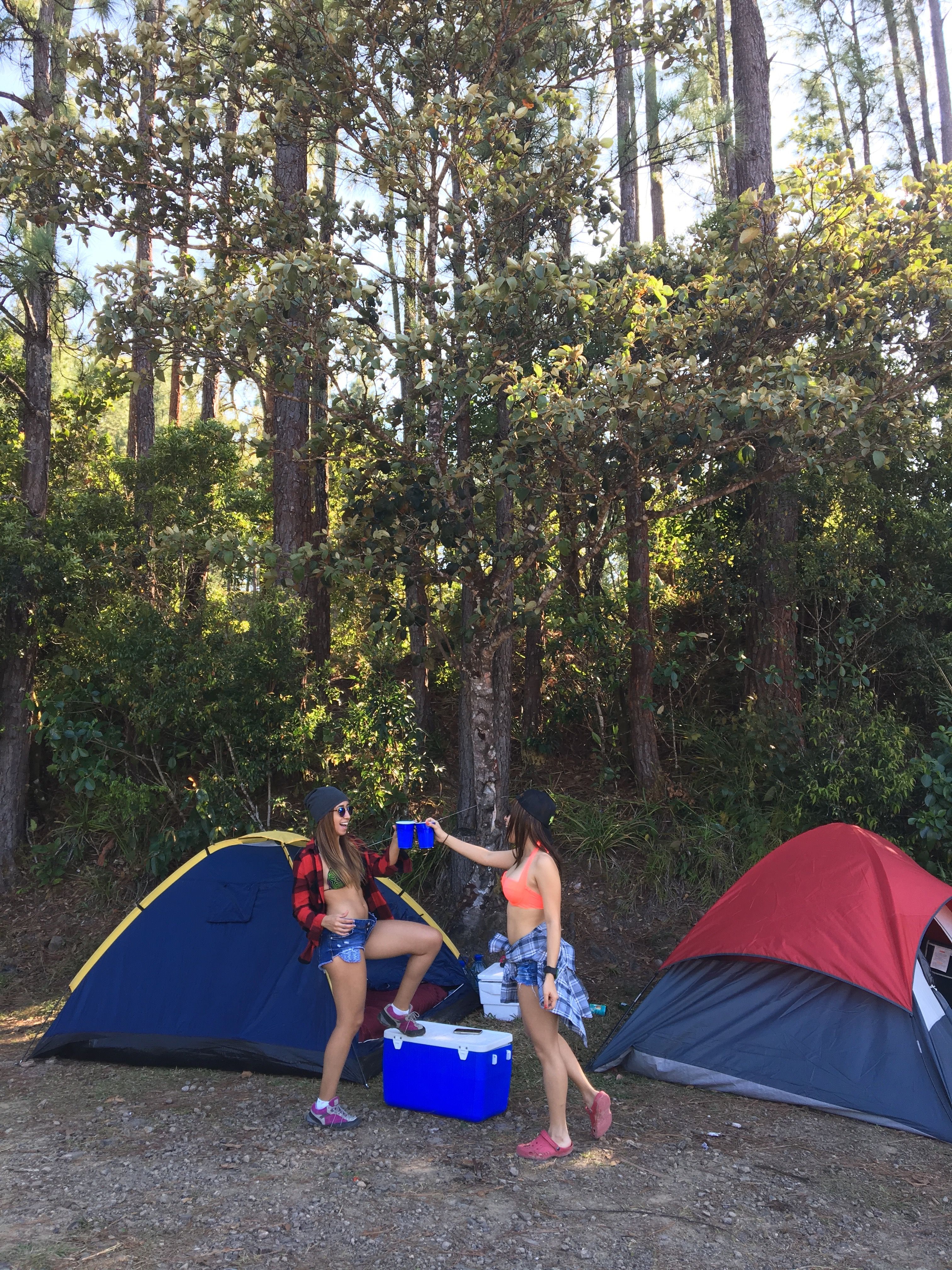 Two women enjoying a camping trip in a forest in Panama with tents and a cooler.