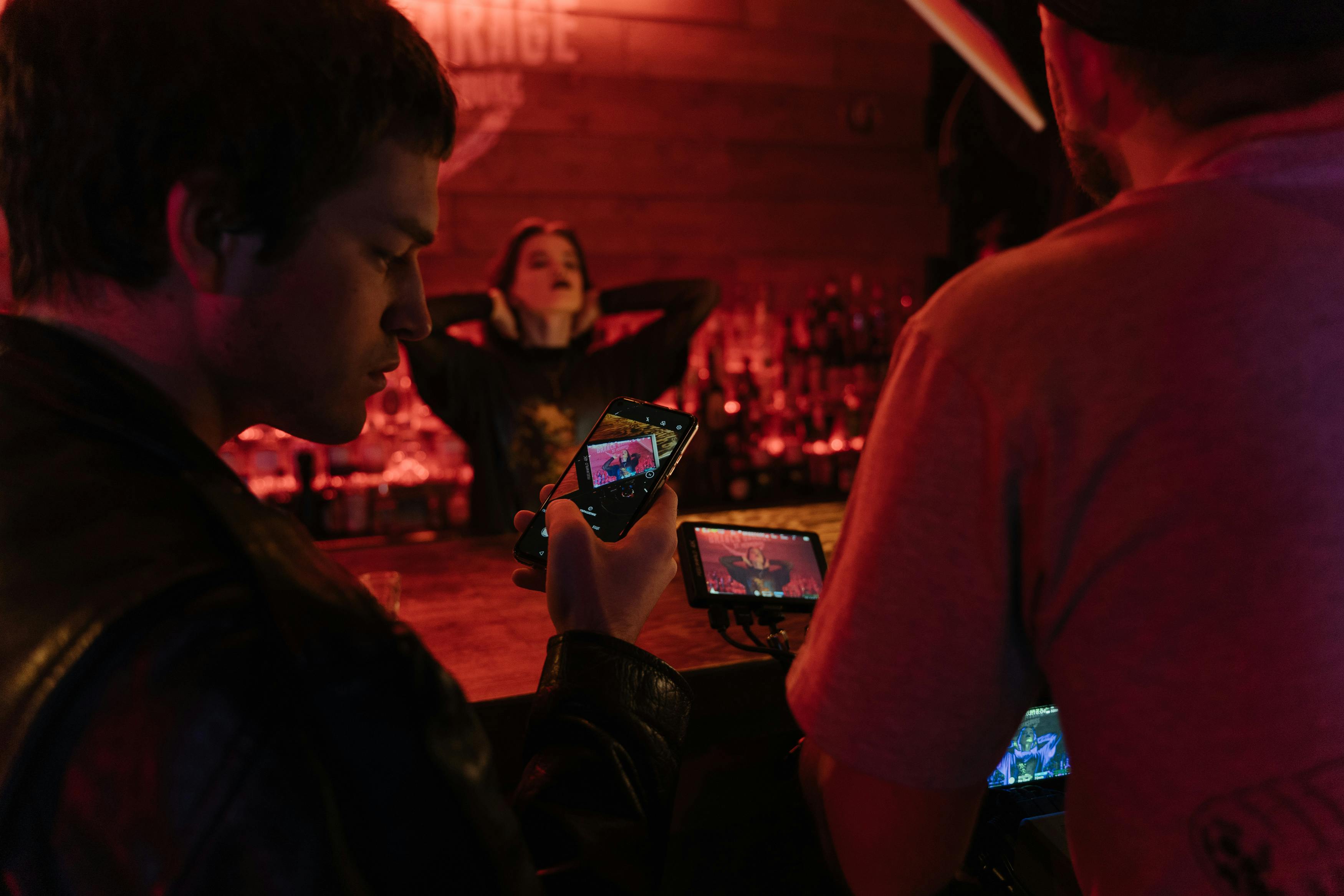 Two men take photos of a woman posing in a vibrant bar setting at night, creating an artistic urban vibe