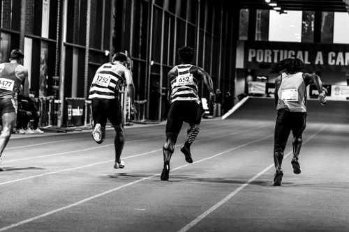 Free Back view of athletes sprinting on an indoor track, captured in grayscale. Stock Photo