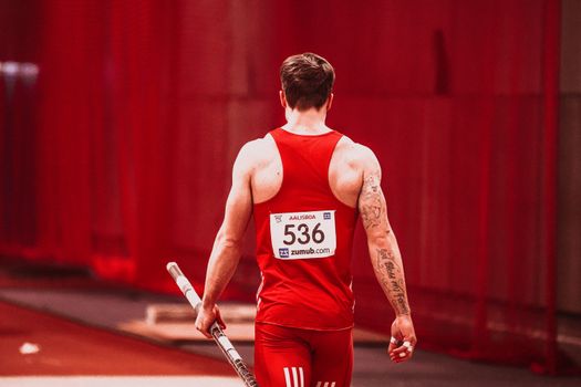 Rear view of male athlete holding pole, ready for vault in red sportswear. — photo by RUN 4 FFWPU