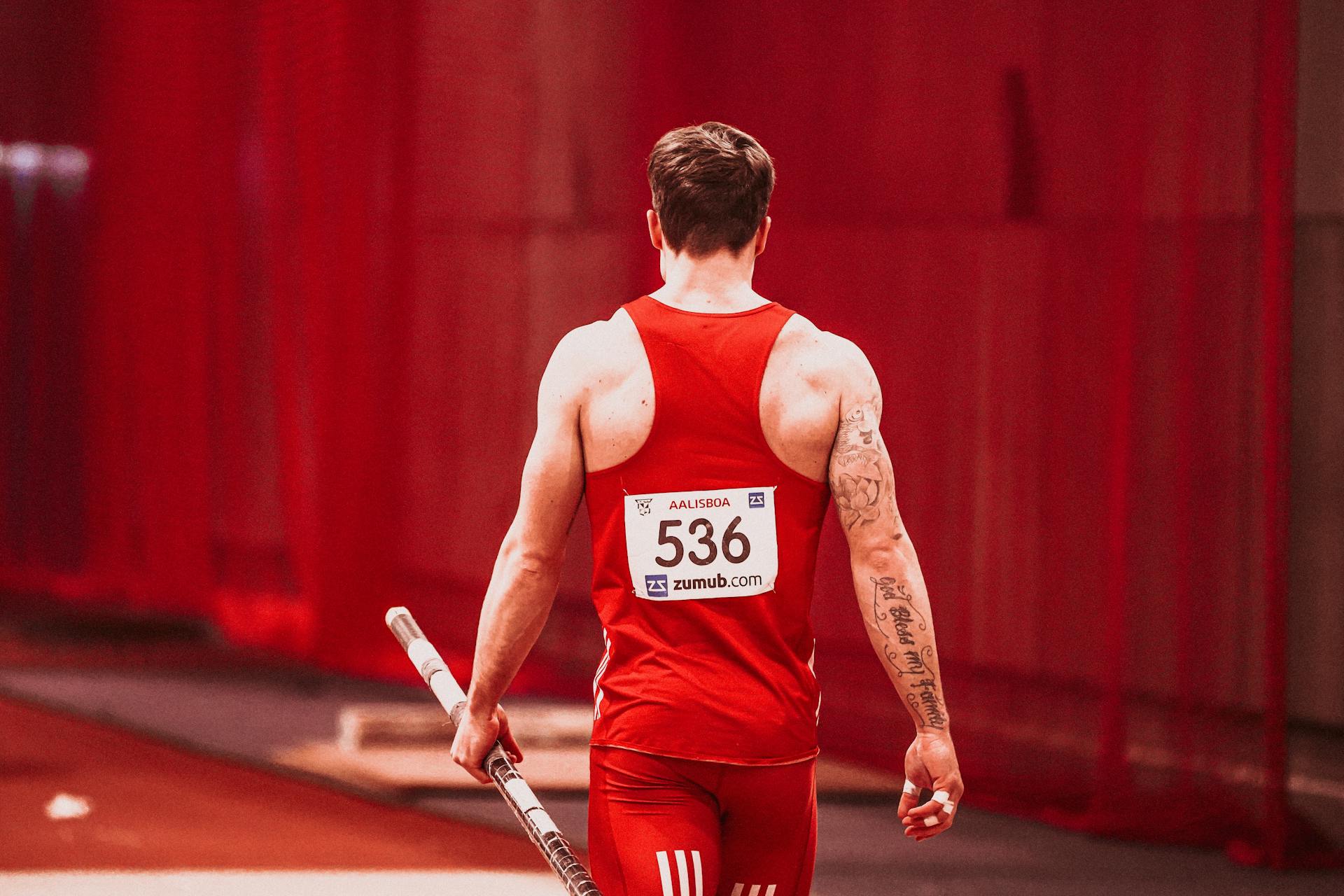 Rear view of male athlete holding pole, ready for vault in red sportswear.