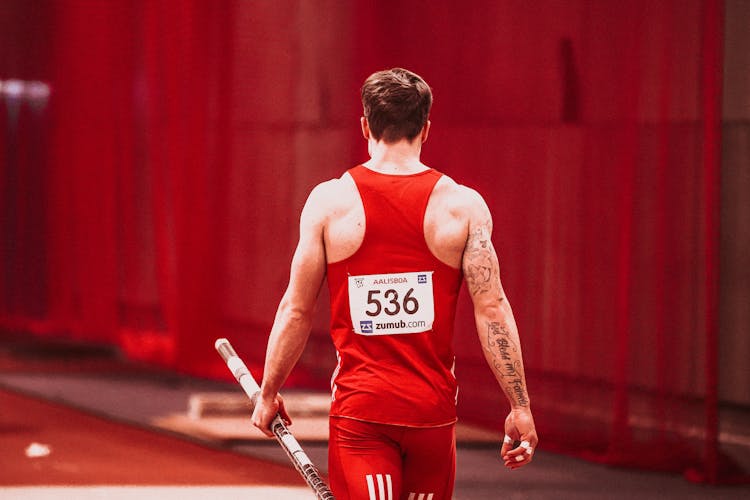 A Man In Red Sports Wear Holding A Pole