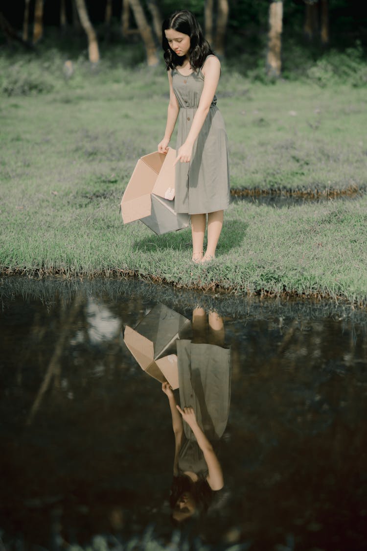 Charming Woman With Cardboard Box Reflecting In Pure Water