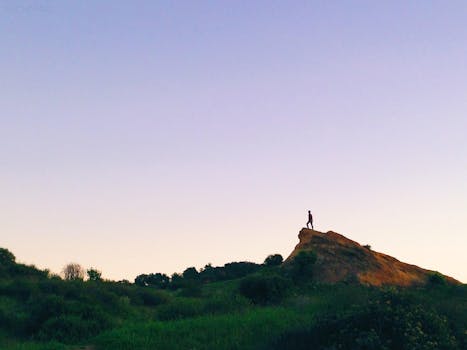 A lone person stands atop a hill under a vast sky, capturing solitude and nature.