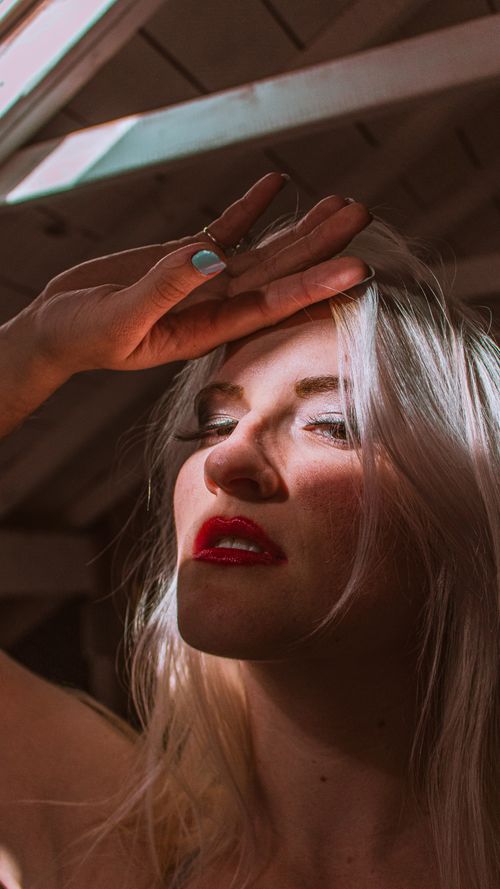 Free Close-up portrait of a blonde woman shading her eyes from sunlight indoors. Stock Photo