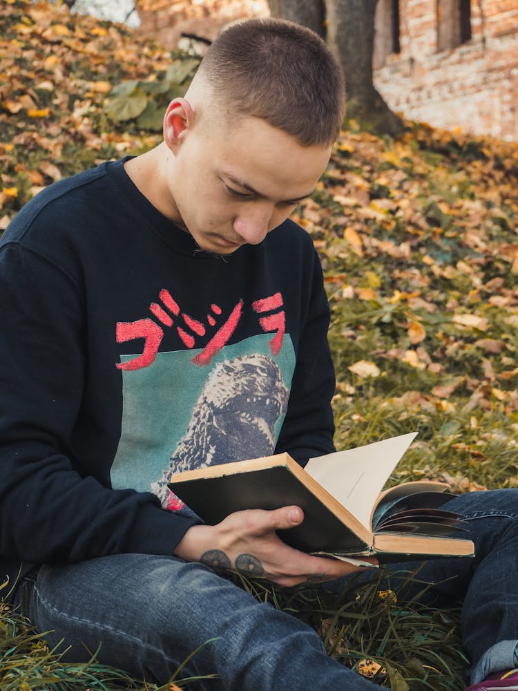 Young Man Sitting On Grass Reading A Book