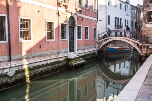 Free Serene canal in Venice with arch bridge and colorful buildings reflecting in the water. Stock Photo