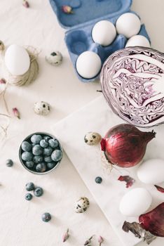 A rustic flat lay with white and quail eggs, blueberries, red cabbage, and onion on a white background.
