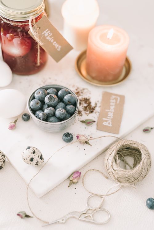 Free Delicate spring-themed still life featuring blueberries, candles, and rustic utensils. Stock Photo