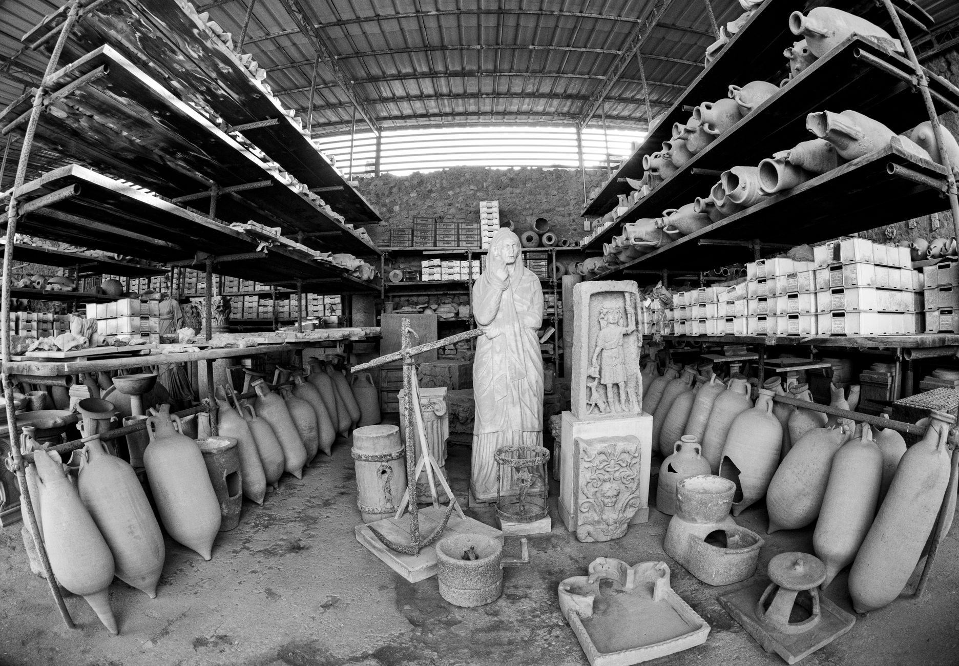 A black and white image of a warehouse filled with clay pots and sculptures, showcasing an industrial setting.