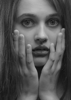 Black and white portrait of a young woman with surprised expression, hands on face.
