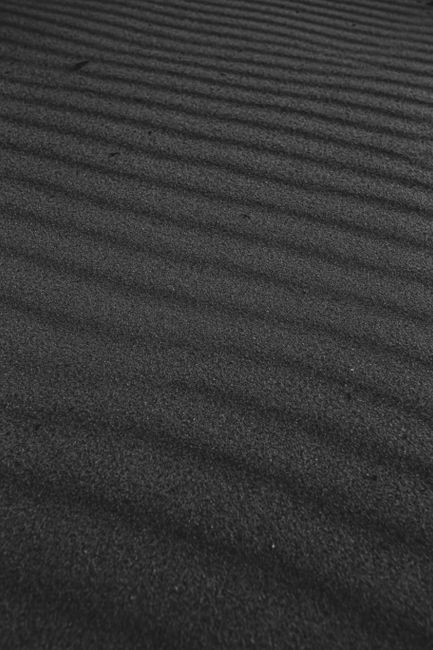 Close-up view of ripple patterns in black sand, showcasing natural texture and stripes.