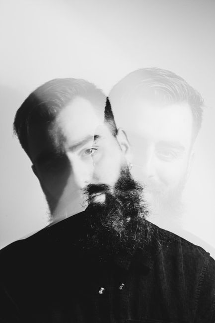 Artistic double exposure portrait of a bearded man in black and white with a modern, conceptual feel.