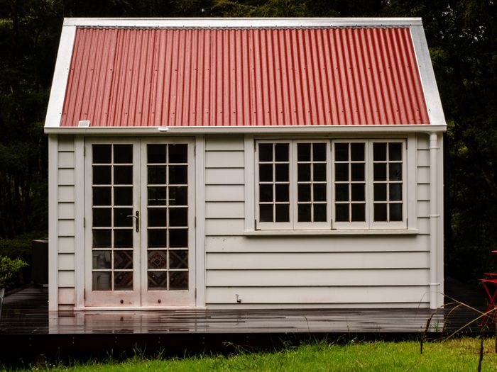 A white timber garden building with French doors and a red roof