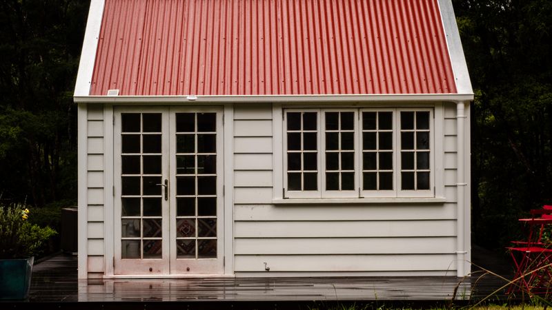 A white timber garden building with French doors and a red roof