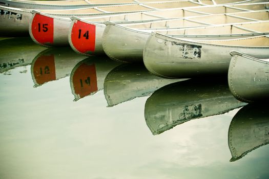 Multiple canoes rest on a calm lake, creating a mirrored reflection in serene outdoor setting.