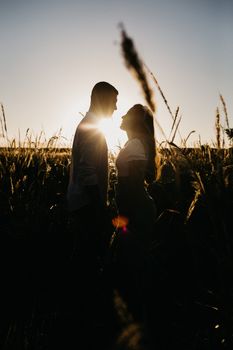 Side view silhouette of unrecognizable couple standing close against bright sunlight in grassy field at sundown