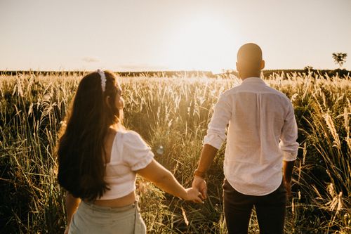 Free Back view of anonymous couple multiethnic couple holding hands standing in grassy meadow in sunny sundown Stock Photo