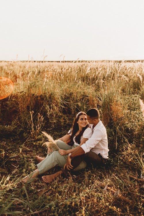 Diverse barefoot gentle couple sitting on grassy ground