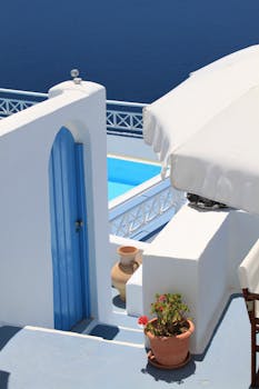 Elegant Santorini architecture featuring a blue door, sea view, and swimming pool under a bright summer sky.