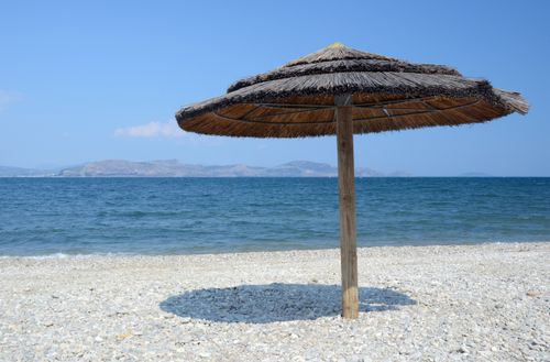 Free Serene pebble beach with straw parasol overlooking the ocean and distant hills. Stock Photo