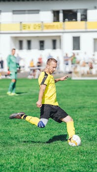 A soccer player in yellow jersey actively kicking the ball on a green field, during a sunny day outdoor match.