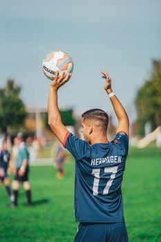 Back view of a soccer player preparing to throw in the ball during a game on a sunny day.
