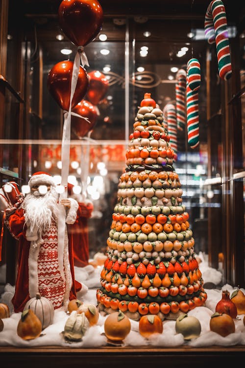 Showcase of triangle shaped sweets stand and Santa figurine placed on artificial snow and decorated with festive baubles