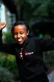 Smiling African woman in a YouTube jacket celebrating outdoors in Nairobi.