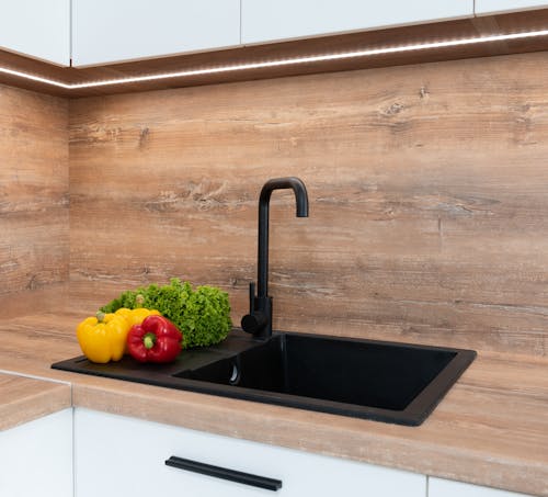 Fresh green lettuce with red and yellow bell peppers placed near sink on wooden tabletop in modern kitchen