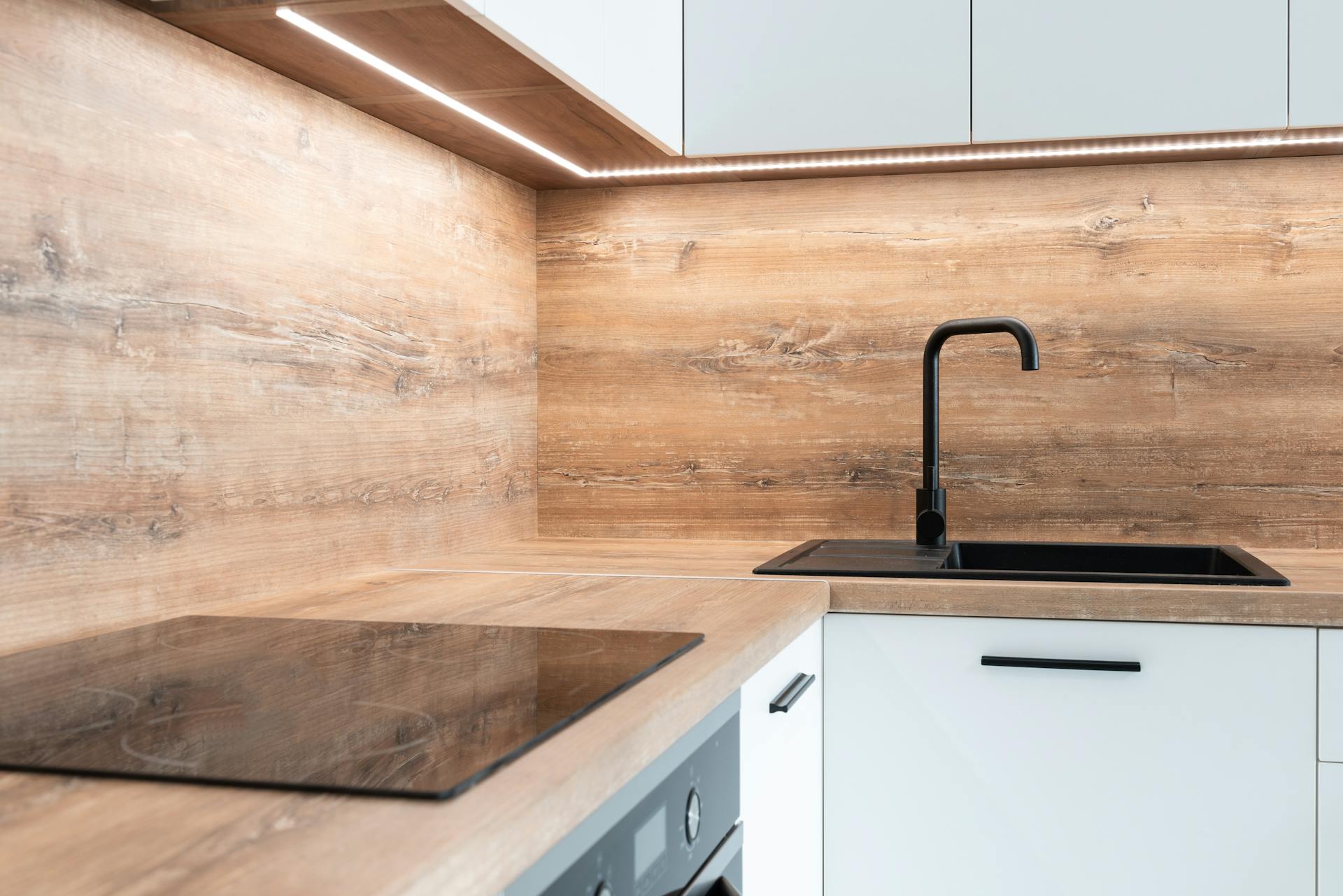 Modern black appliance and sink with faucet in stylish kitchen with wooden walls and white furniture