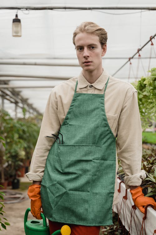 Man in Green Apron with Orange Gloves Holding a Watering Can